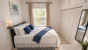 Un dormitorio con cama, mesita de noche, lámpara, ventana con cortinas, espejo, armario y una planta.