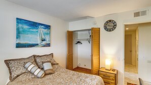Ein Schlafzimmer mit Bett, Gemälde, Kleiderschrank, Nachttisch mit Lampe und einer Uhr an der Wand.