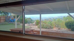 Eine überdachte Terrasse mit Blick auf einen Garten, ein Holztisch und ein Zaun.