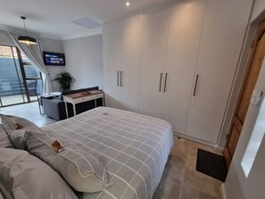 A bedroom with a bed, a desk, a TV, and a wardrobe. - Saxon Guest Cottage Suite (Cape Town)