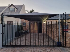 A gated entrance with a brick wall, a metal gate, and a roofed area. - Saxon Guest Cottage Suite (Cape Town)