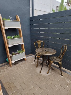 A small outdoor patio with a metal table and chairs, a wooden ladder with planters, and a dark fence. - Saxon Guest Cottage Suite (Cape Town)