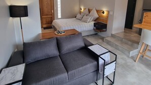 A modern bedroom with a bed, bedside tables, a ceiling fan, and a view of the adjacent living area. - Saxon Guest Cottage Suite (Cape Town)
