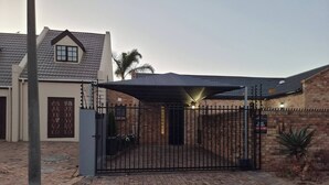 A gated residential property with a brick wall, a metal gate, and a covered driveway. - Saxon Guest Cottage Suite (Cape Town)