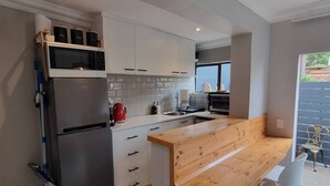 A modern kitchen with a built-in microwave, a stainless steel refrigerator, and a wooden island with seating. - Saxon Guest Cottage Suite (Cape Town)