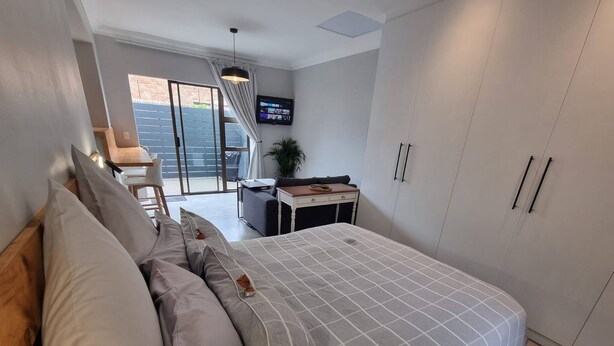 A modern bedroom with a bed, a desk, a TV, and a balcony. - Saxon Guest Cottage Suite (Cape Town)