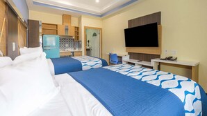 A hotel room with two beds, a kitchenette, a TV, and a desk.