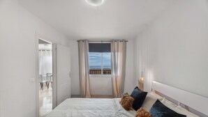 Un dormitorio con cama, cortinas, una ventana con vistas y una lámpara de noche.