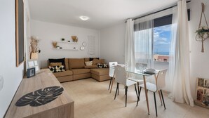 Un salón moderno con una mesa de comedor de vidrio, sillas blancas, un sofá color beige y vistas al mar a través de grandes ventanales.