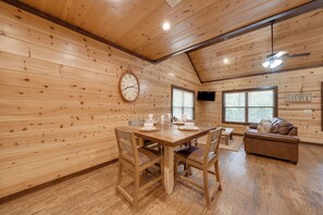 Ein Holzinterieur mit Esstisch, Stühlen, einer Couch, einem Deckenventilator und einer Wanduhr.