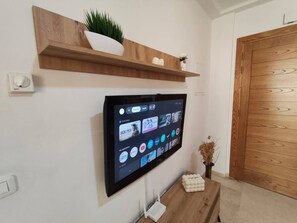 Ein flachbildfernseher an der Wand, darüber ein Holzregal und ein kleiner Tisch mit einem dekorativen Gegenstand.