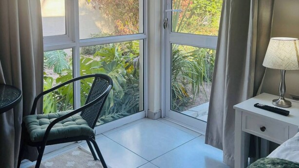 Una habitación con un gran ventanal corredizo, una cama, una silla, una mesita y una lámpara.