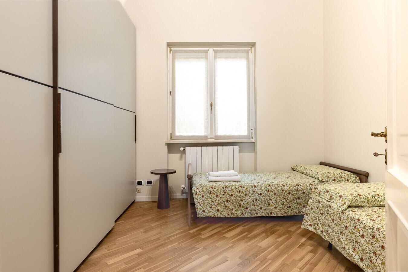 A small bedroom with a bed, a radiator, a window, and a wardrobe.