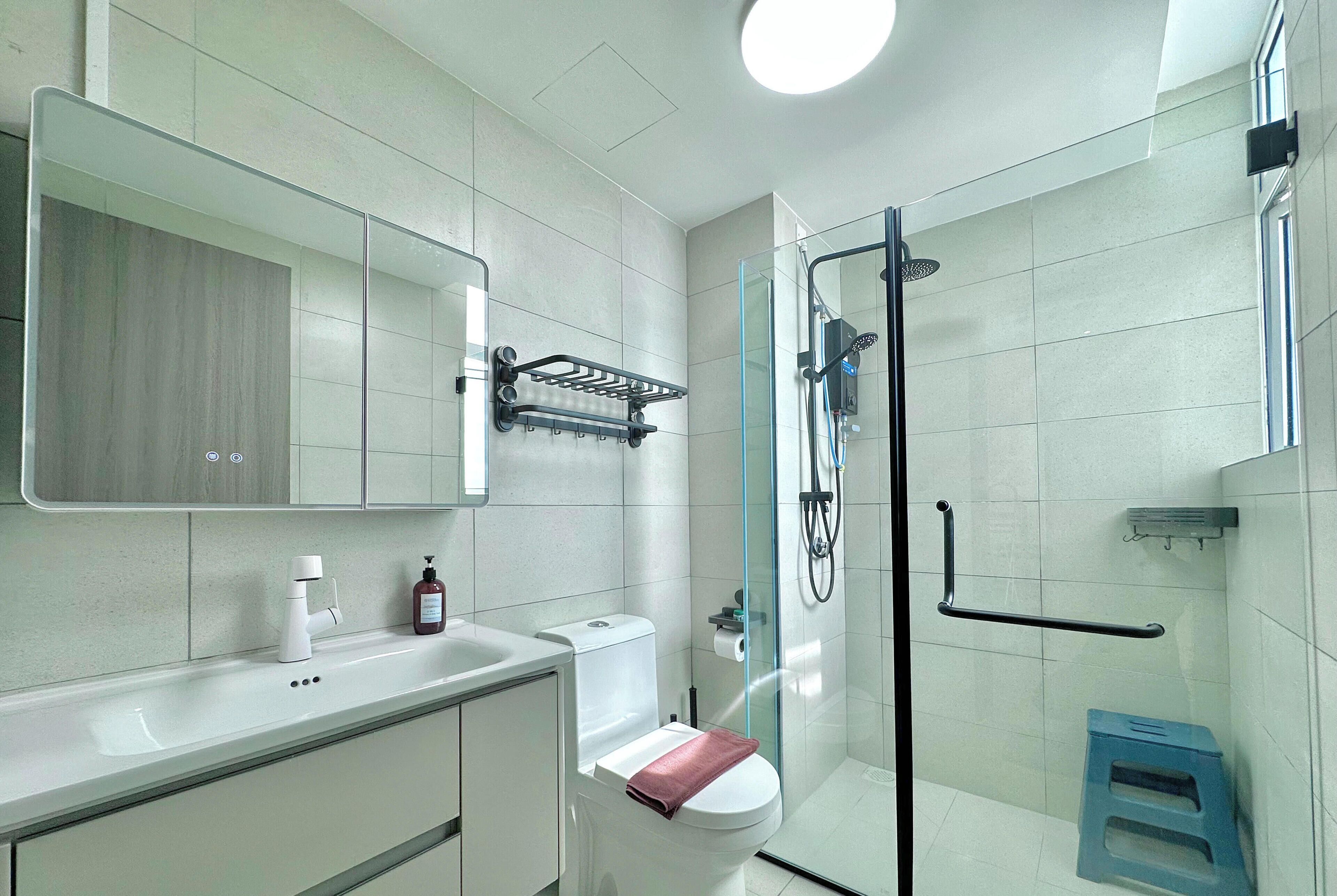 A modern bathroom with a glass shower enclosure, a white toilet, and a sink with a soap dispenser.