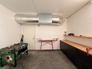 Une pièce avec une table de baby-foot, une table pliante rouge et une étagère remplie d’outils.