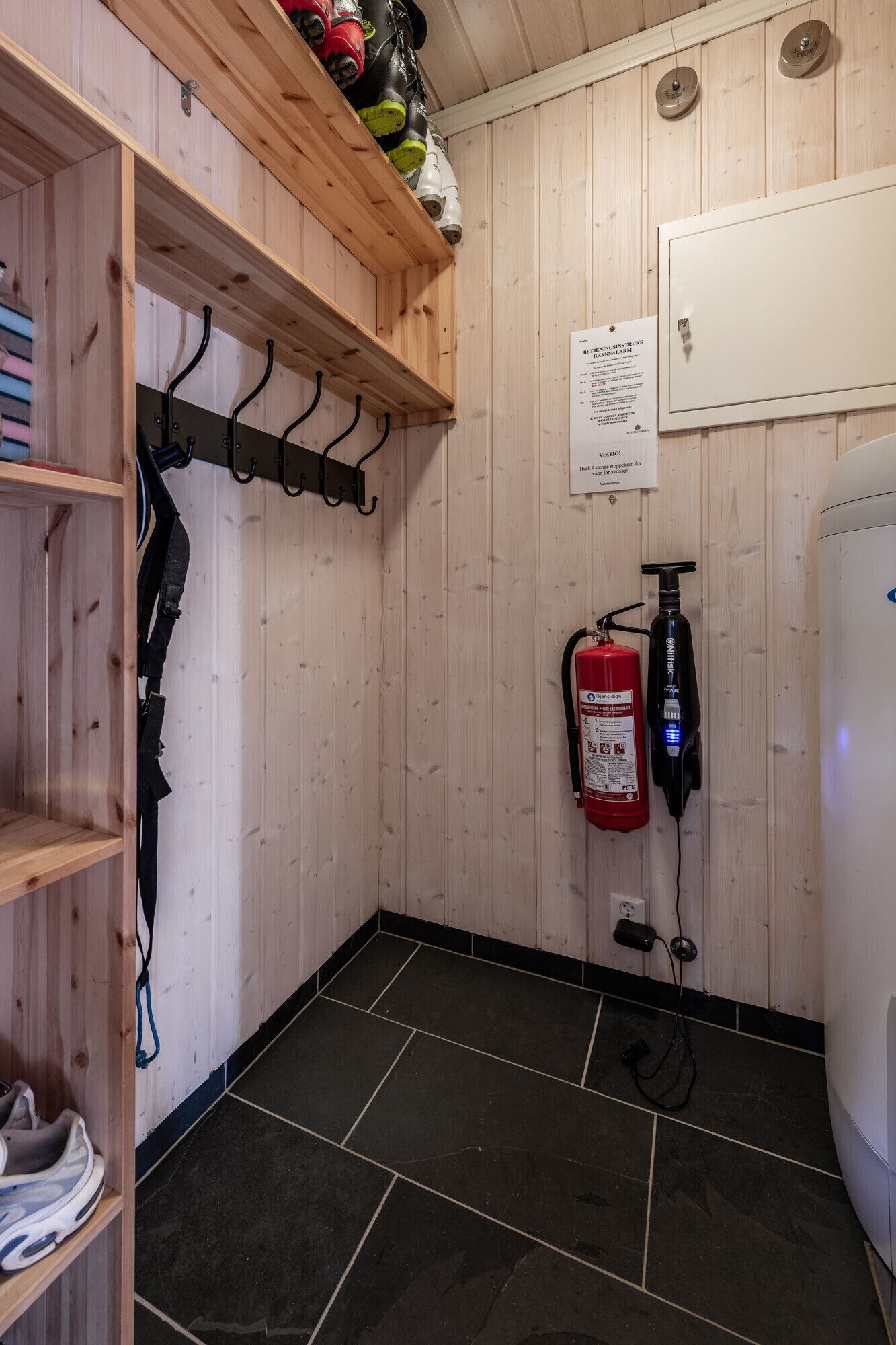 A small, enclosed space with a wooden interior, a fire extinguisher mounted on the wall, and a shelf with boots.