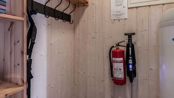 A small, enclosed space with a wooden interior, a fire extinguisher mounted on the wall, and a shelf with boots.