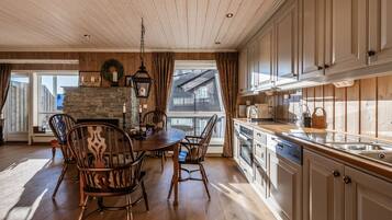 A dining area with a stone fireplace, wooden ceiling, and a view of a house through a window.