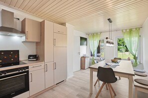 Eine moderne Küche mit Einbauofen, eine Essecke mit Tisch und Stühlen sowie ein Blick ins Freie durch ein Fenster.