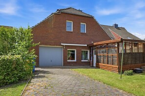 Ein zweistöckiges Backsteinhhaus mit Garage, überdachter Veranda und Garten.
