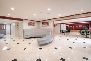 Eine Hotelhalle mit einer gebogenen Sitzgruppe, einem Empfangsbereich und einem Essbereich mit Tischen und Stühlen.