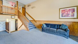A staircase with wooden railings, a blue carpeted floor, a gray sofa with pillows, and a framed picture on the wall.