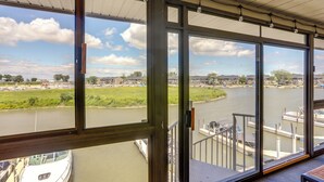 Uitzicht vanuit een kamer met grote ramen op een rivier, boten en een verafgelegen stadsbeeld.