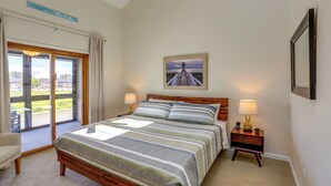 Een slaapkamer met een bed, twee nachtkastjes met lampen, een lijst met een afbeelding aan de muur en uitzicht op de omgeving door een schuifdeur.