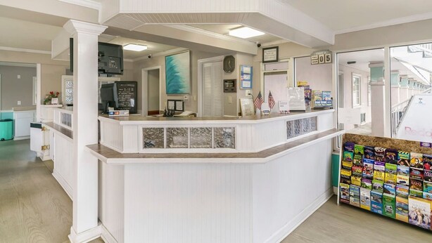 A reception area with a white counter, a clock, a framed picture, and a magazine rack. - Myrtle Beach SC | 3 full bed (Myrtle Beach SC)