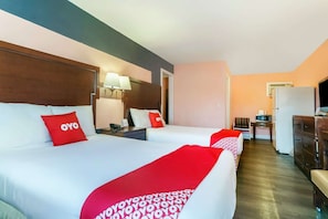 Una camera d'albergo con due letti, una scrivania, un frigorifero e un televisore.