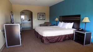 Une chambre d’hôtel avec un lit, des tables de chevet, un bureau, une chaise, un miroir et une salle de bain visible au fond.