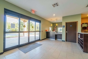 A hotel lobby with a reception desk, a 'Welcome' sign, an 'EXIT' sign, and a view of the outside. - King Bed|Non-Smoking (Moulton, TX)
