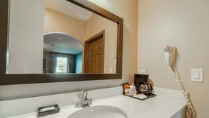 Une salle de bain équipée d’un lavabo, d’un miroir, d’un sèche-cheveux et d’une machine à café.