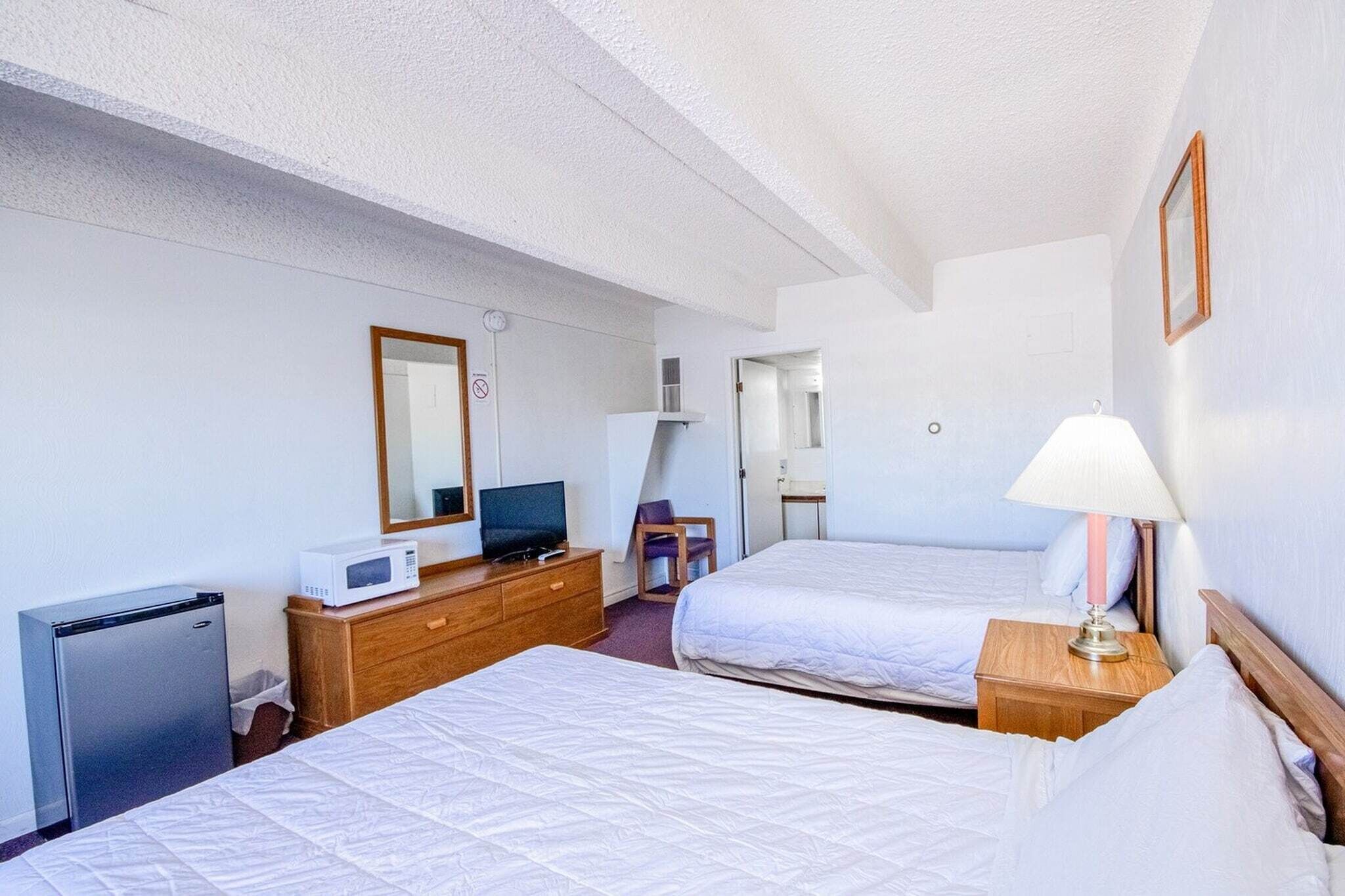 Een hotelkamer met twee bedden, een bureau met een computer, een magnetron en een kleine koelkast.