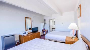 Een hotelkamer met twee bedden, een bureau met een computer, een magnetron en een kleine koelkast.