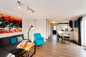 Ein modernes Wohnzimmer mit einer Couch, einem Couchtisch, einem hellblauen Sessel und einem Essbereich mit Tisch und Stühlen.