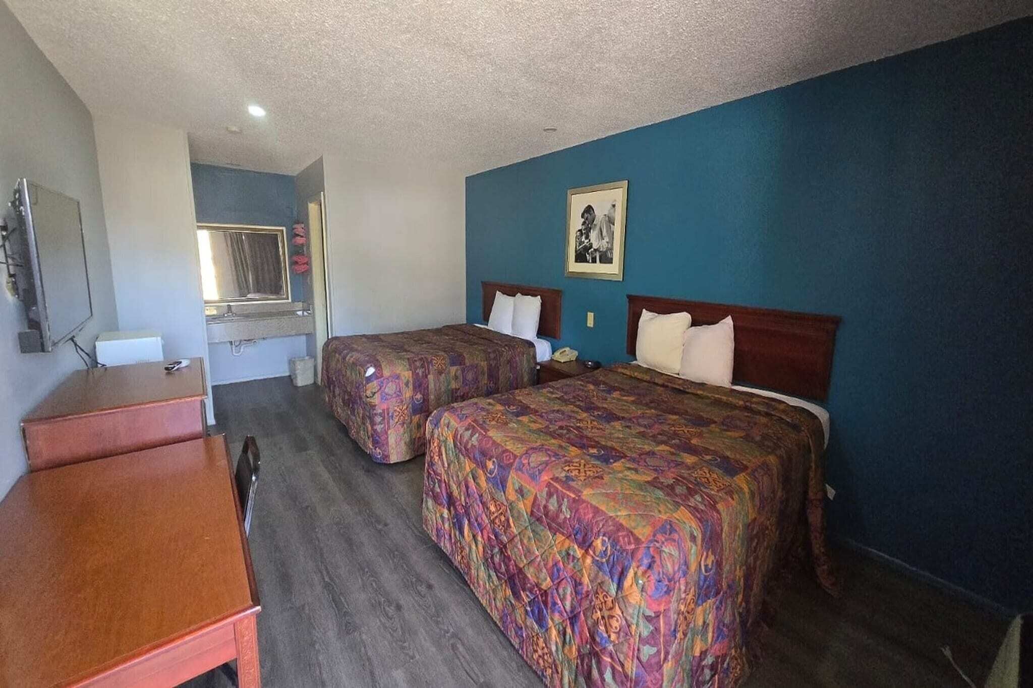 A hotel room with two beds, a desk, a mirror, and a picture on the wall.