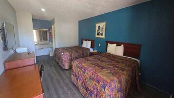 A hotel room with two beds, a desk, a mirror, and a picture on the wall.