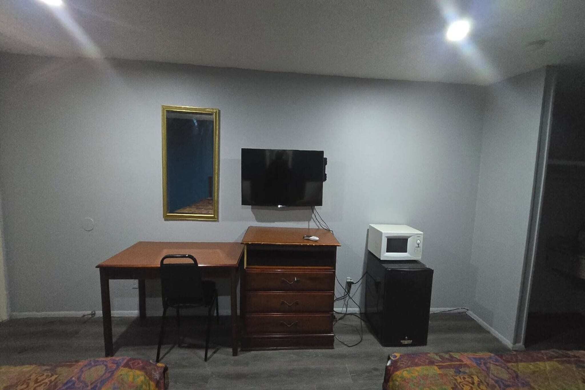 A room with a wooden desk, a chair, a television, a microwave, and a dresser.