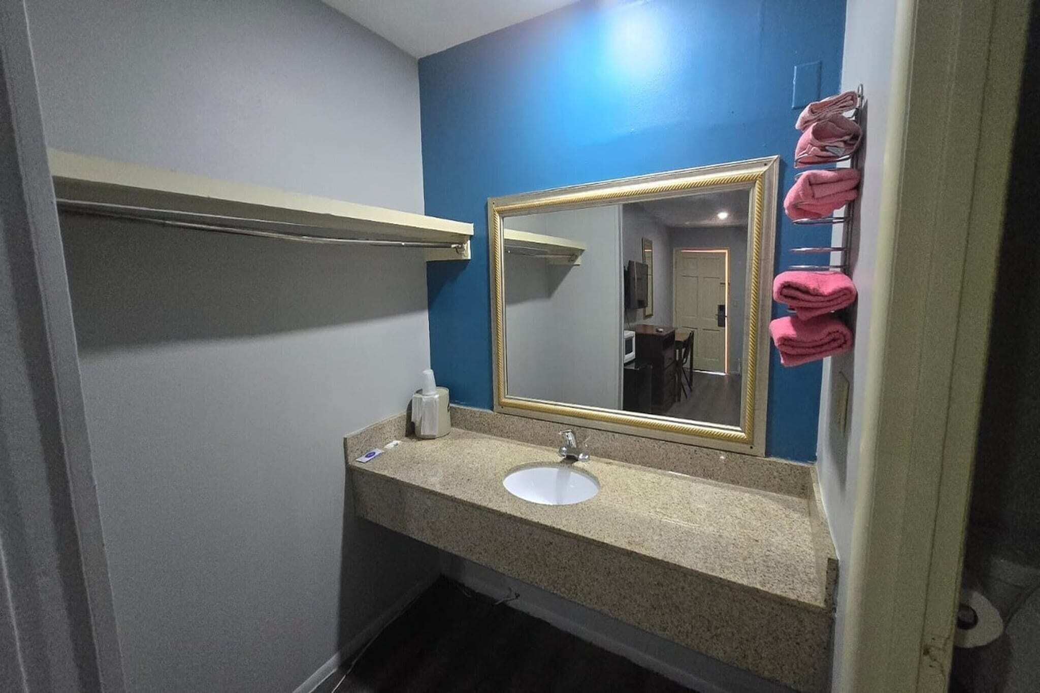A bathroom with a sink, mirror, towel rack, and a door leading to another room.