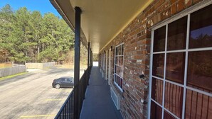 A covered outdoor area with a brick building, a car parked in the background, and a view of trees. - King Bed Non-Smoking (Prentiss, MS)