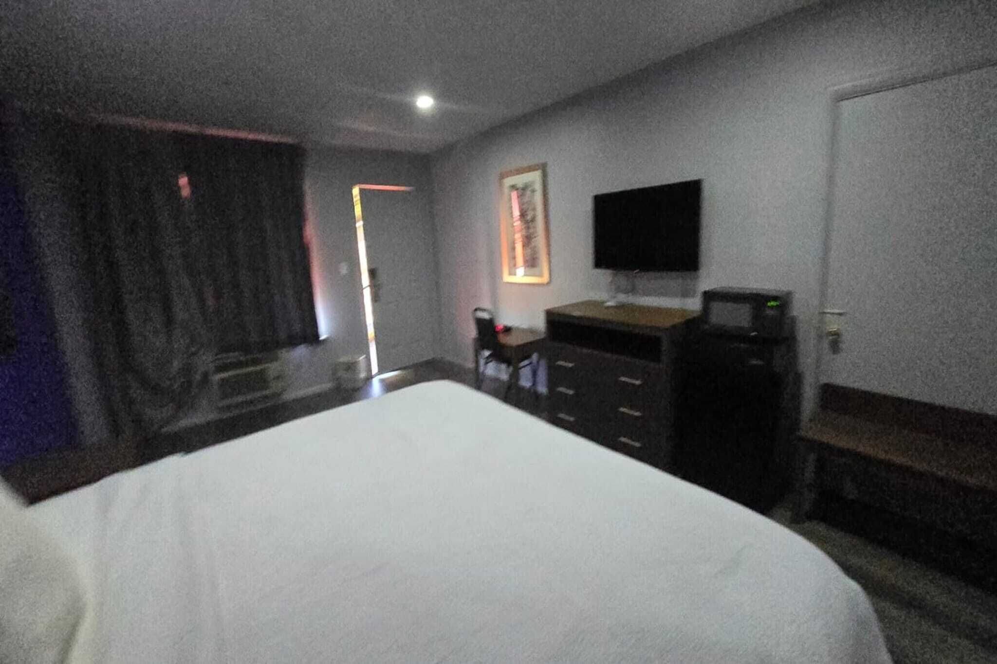 A hotel room with a bed, a desk with a computer, a television, and a door.