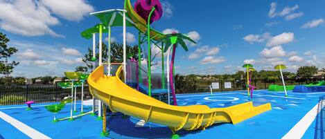 A water park with a yellow slide, green and purple play structures, and a blue pool area.