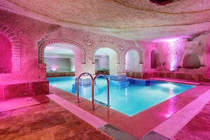 A swimming pool with arched entryways, stone walls, and a tiled floor.