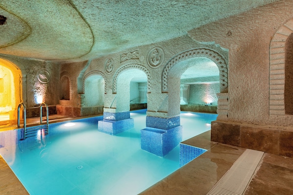 An indoor swimming pool with blue-tiled steps and stone arches.