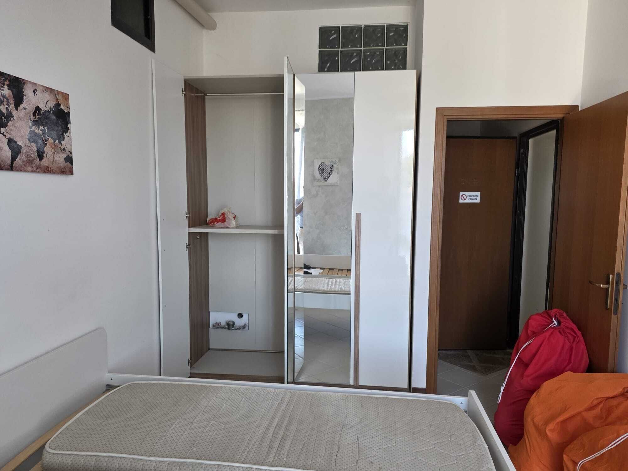 Una habitación con una cama, un armario, un espejo y una puerta.