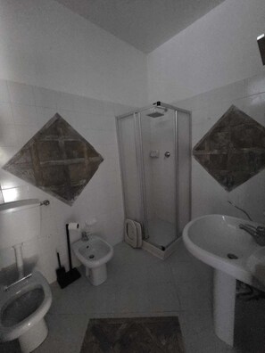 A bathroom with a toilet, bidet, shower, and sink.
