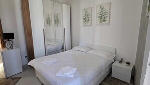 Un dormitorio con cama, armario, mesita de noche y dos láminas botánicas enmarcadas en la pared.