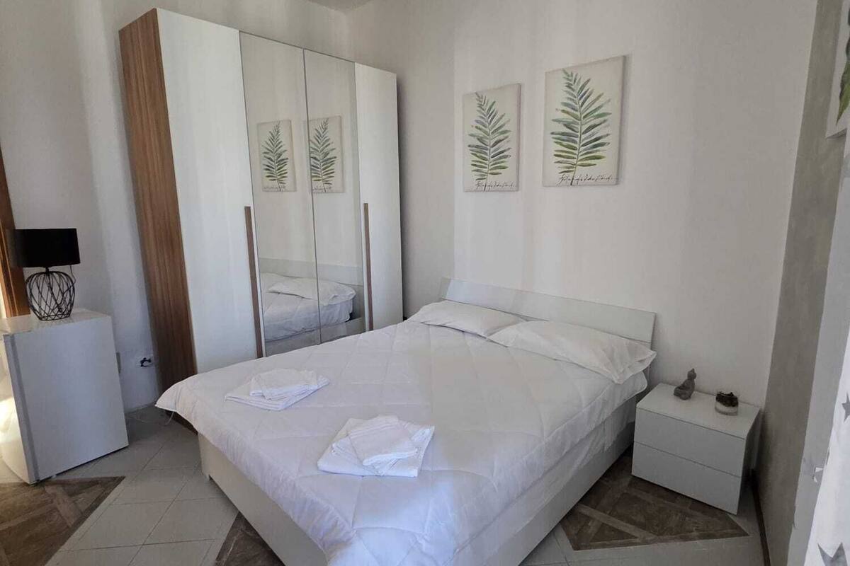 A bedroom with a bed, a wardrobe, a nightstand, and two framed botanical prints on the wall.