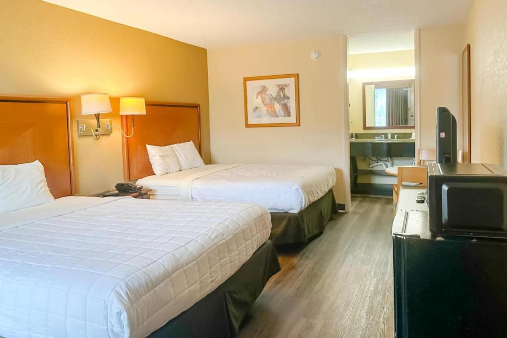 Une chambre d’hôtel avec deux lits, un bureau avec un ordinateur, un téléphone et un miroir.